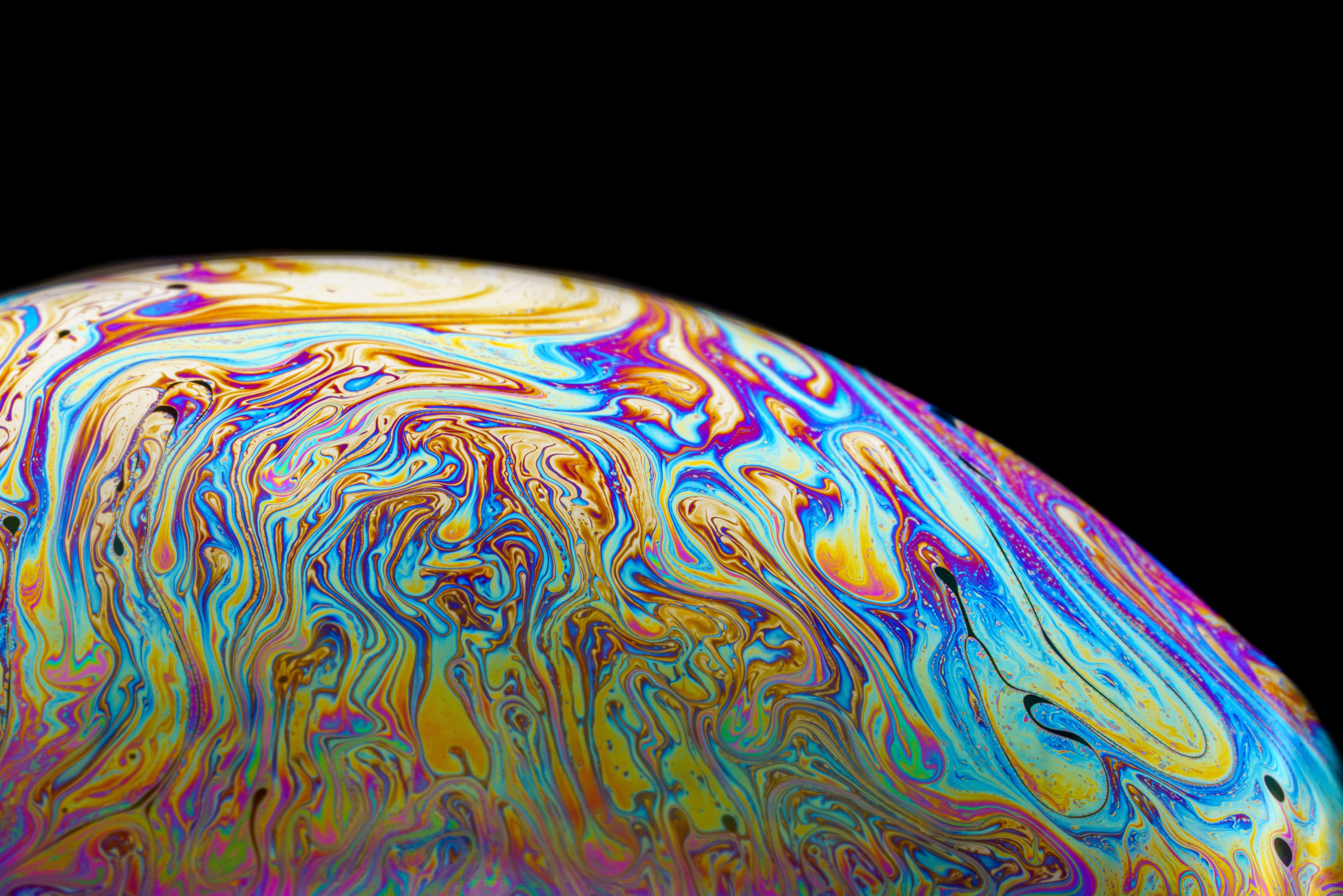 A close up image of the rainbow swirl a soap bubble makes in the right light. Against a black background.