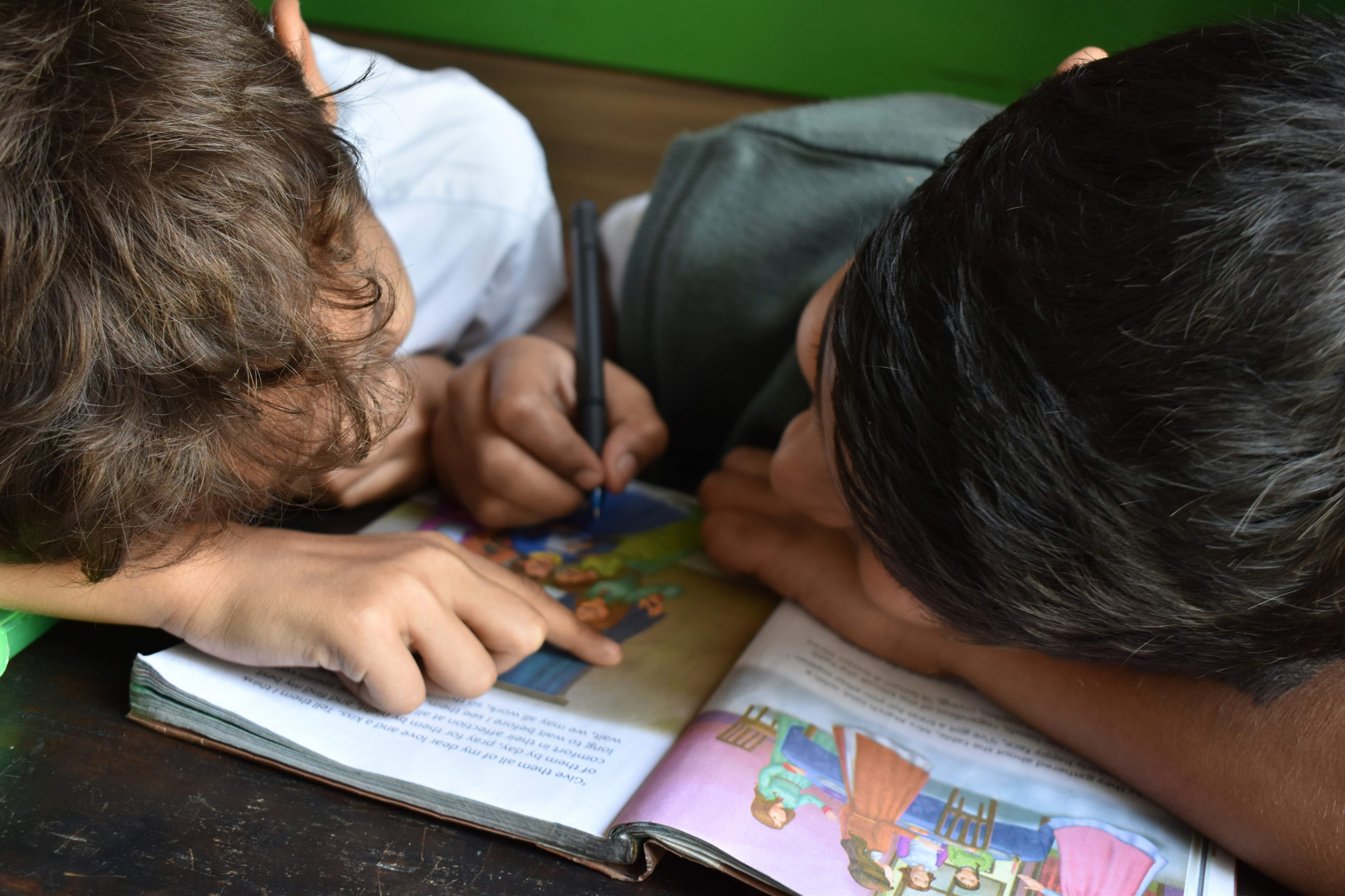Two kids reading and writing in a workbook. Their faces are turned away from the camera.